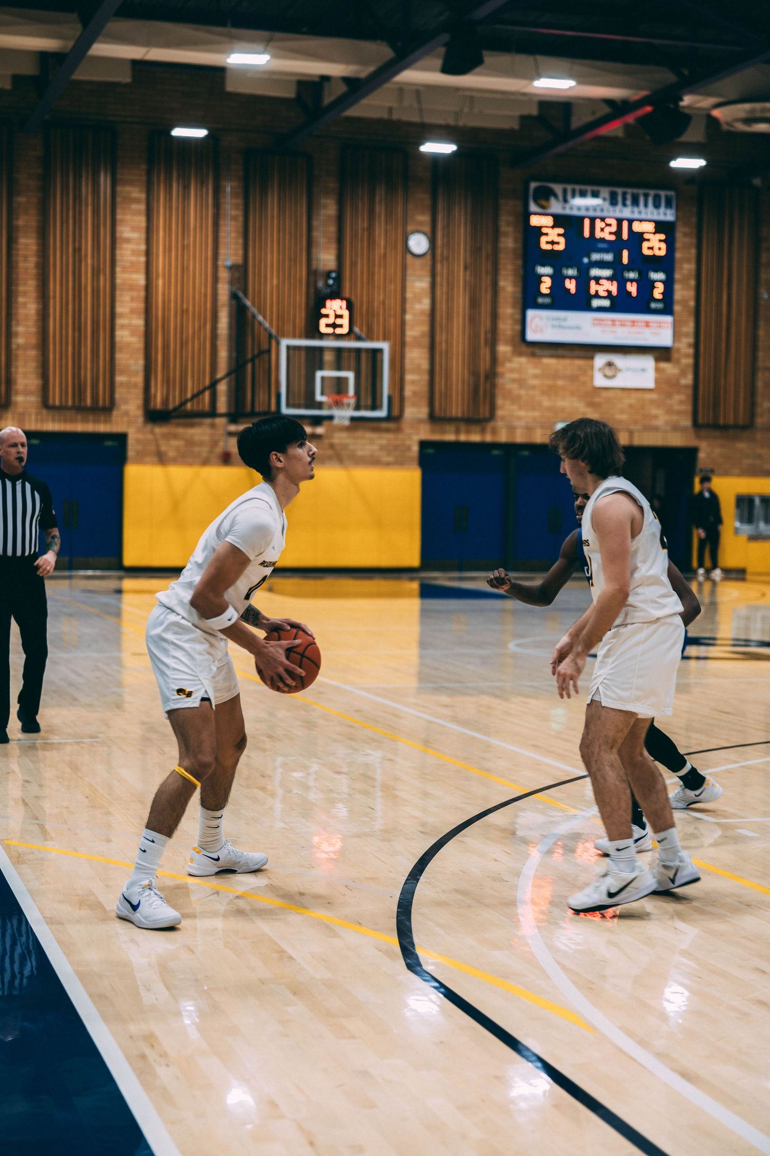 Basketball players practicing dribbling drills on a gymnasium court with yellow and blue walls.