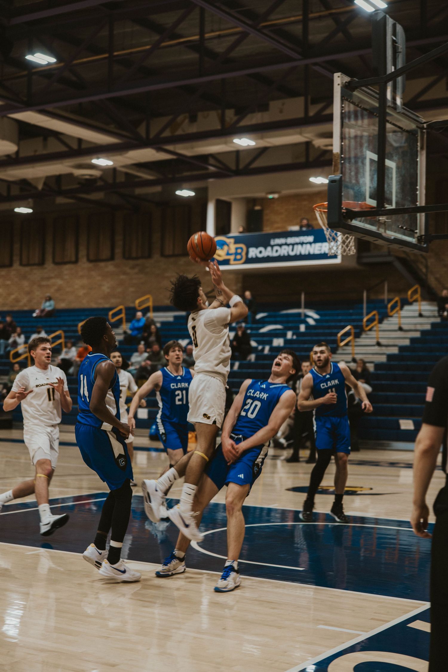 Basketball players in white and blue jerseys competing intensely during a game on indoor court.