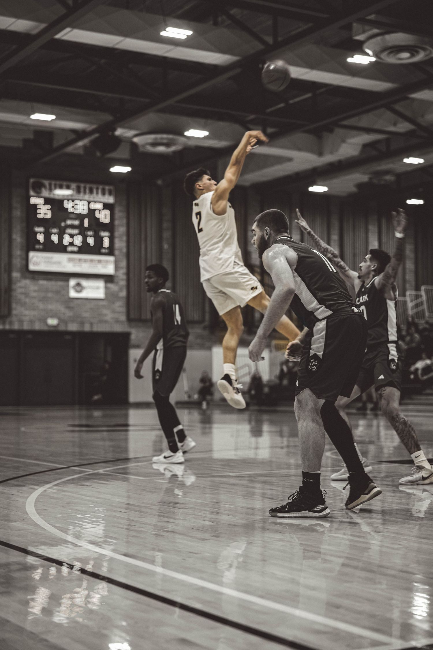 Basketball player in white jersey leaps high for a shot during an indoor game.