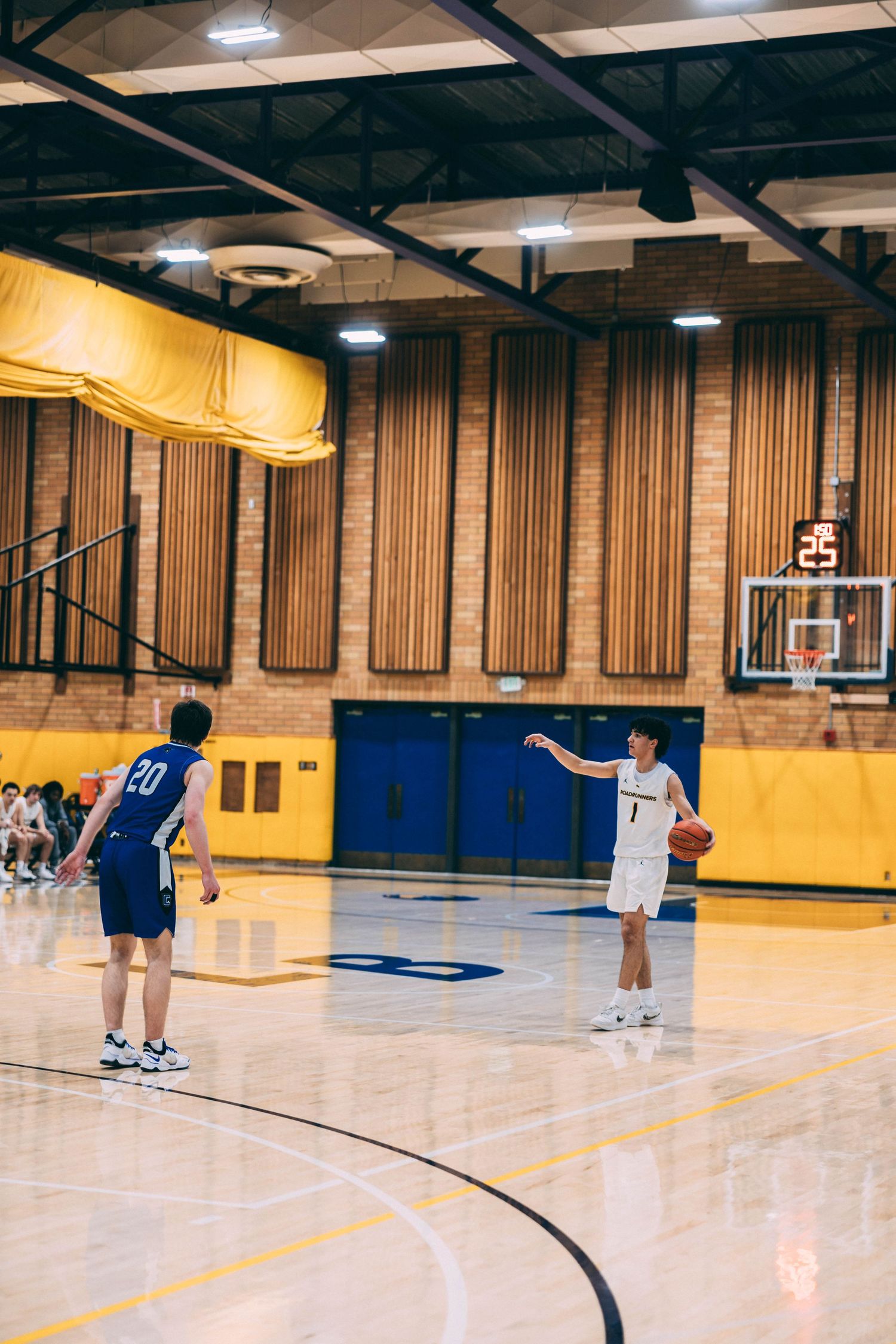 Wide view of basketball gymnasium showing players spread across court during practice.