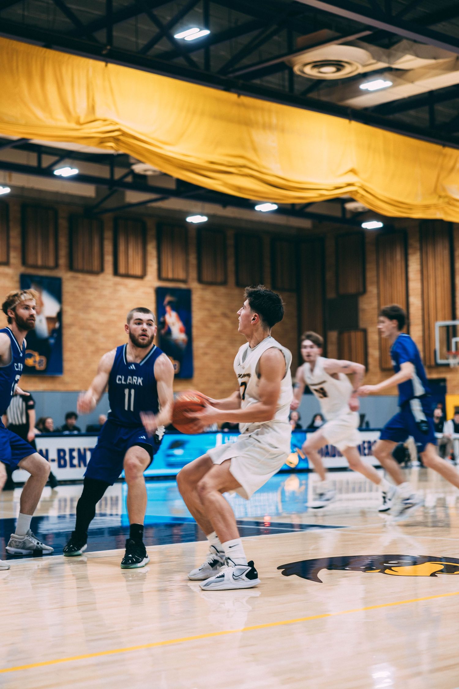 Basketball players performing defensive sliding drills across gymnasium floor.
