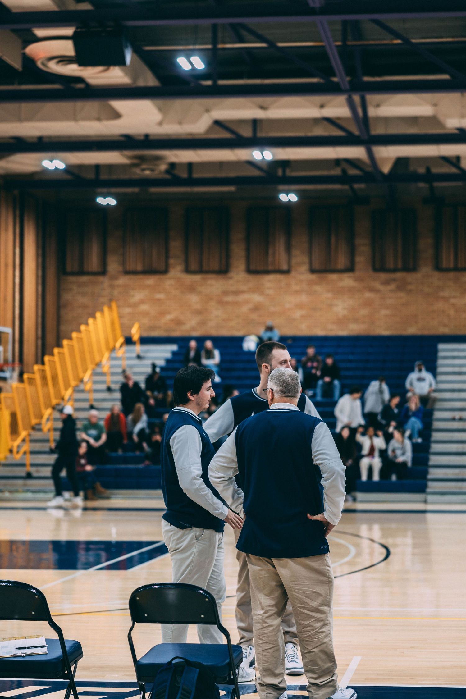 Two coaches discuss strategy while standing courtside during a basketball game.