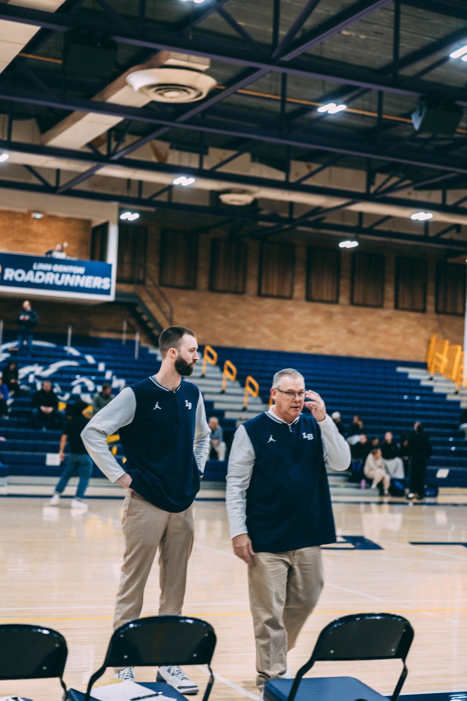Basketball officials and coaches discuss on the sideline of a high school gymnasium during a game.
