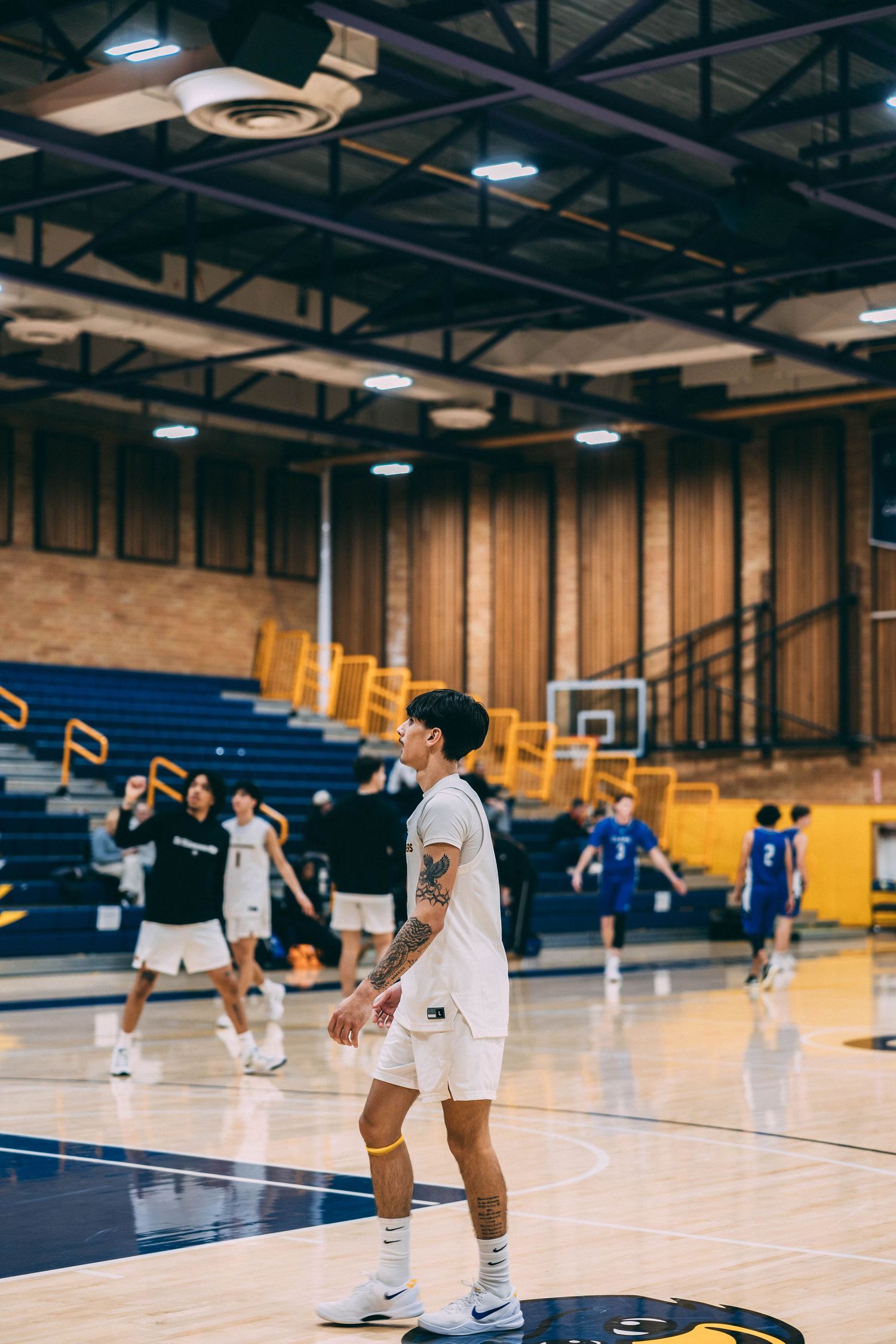 Players warm up on a basketball court with blue and yellow accents before a game.
