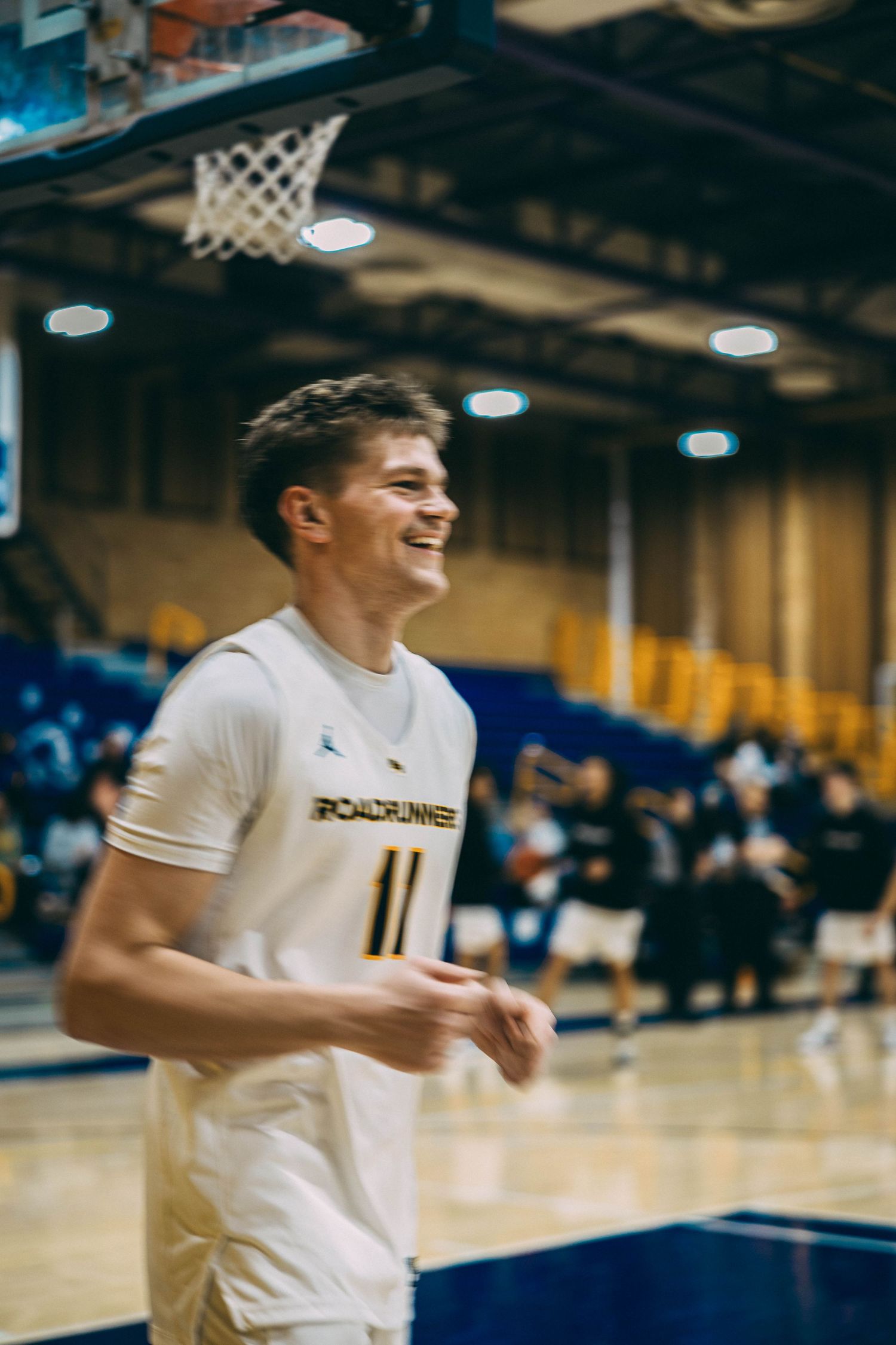 Basketball player in white jersey smiles during a game in an indoor gymnasium.