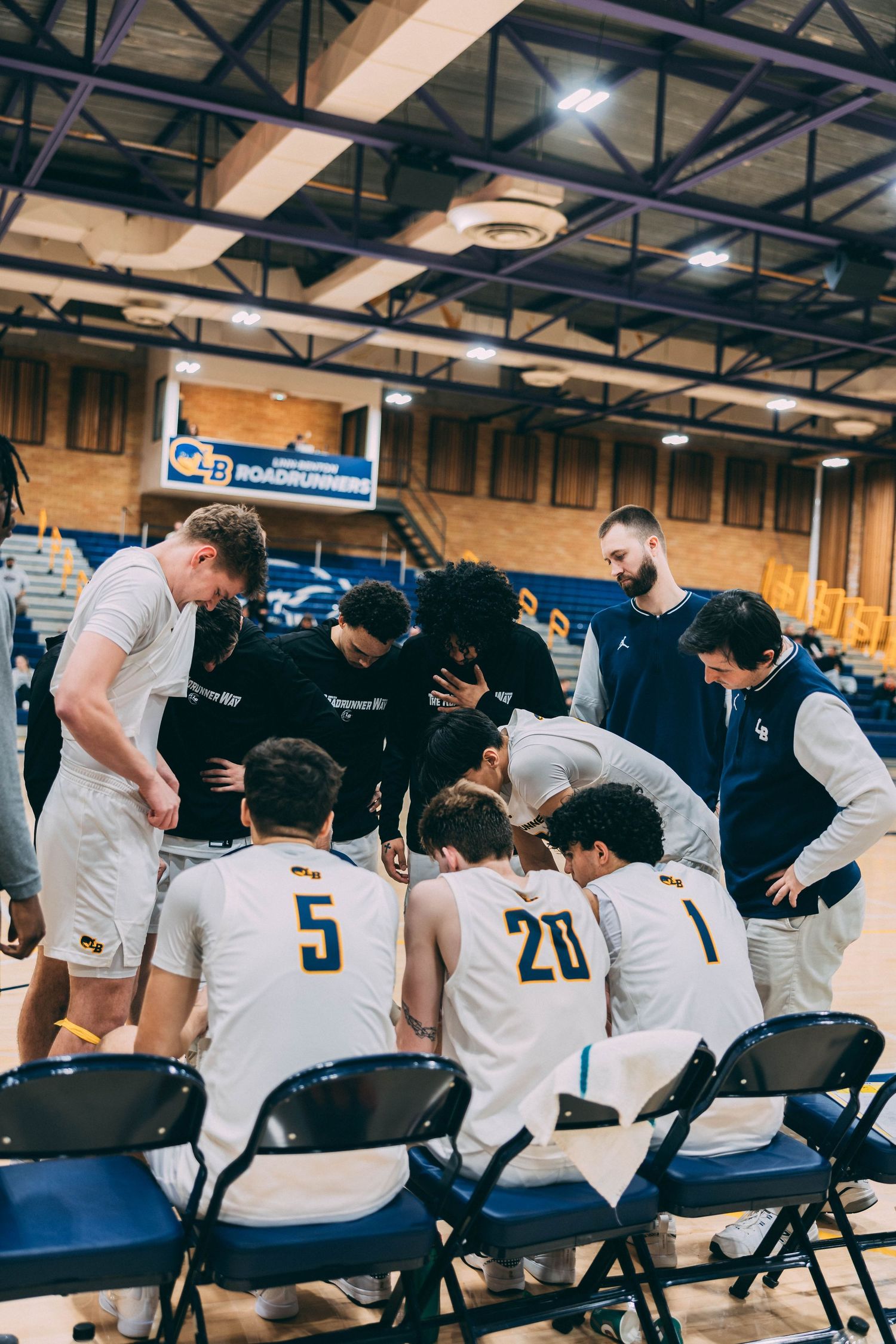 Team members sit on folding chairs along the sideline during a basketball game.