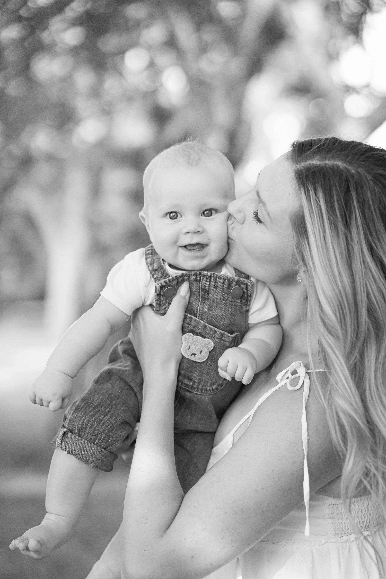 Tender moments between parent and baby captured in black and white outdoor portraits.