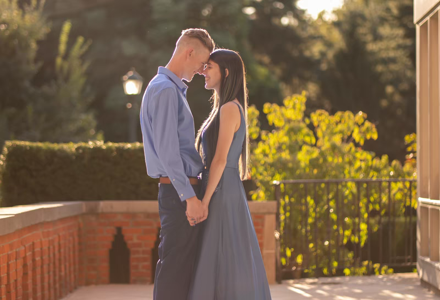 A couple embraces near a brick wall during golden hour with sunflowers in the background.