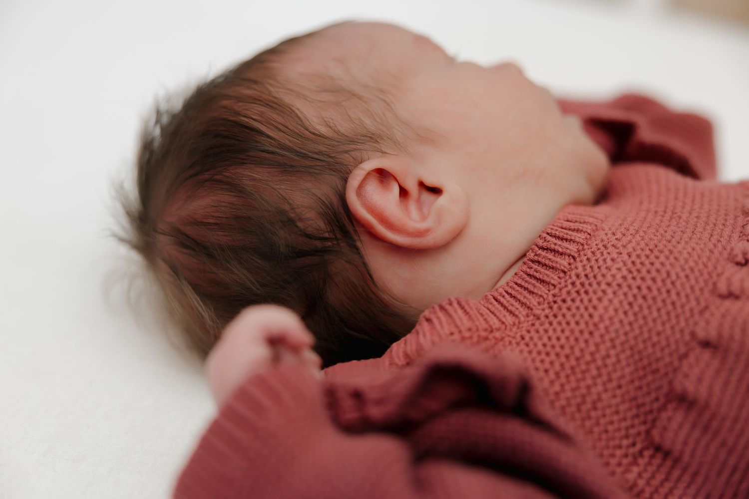 A collection of images showing a sleeping baby wearing a rust-colored knit sweater in various poses.