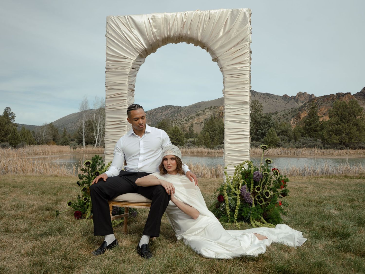 A wedding photo setup with white draped fabric backdrop, decorative parasol, and chair arranged in an outdoor garden setting.