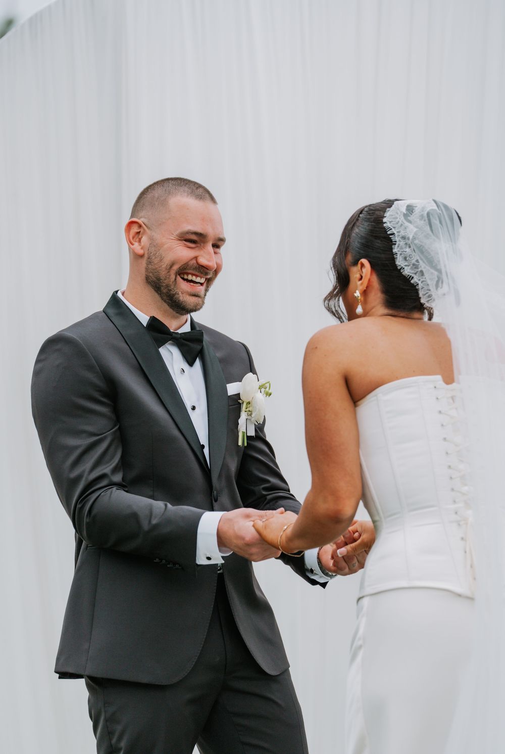 Candid moments of a couple sharing joyful laughter during their wedding celebration against a white backdrop.
