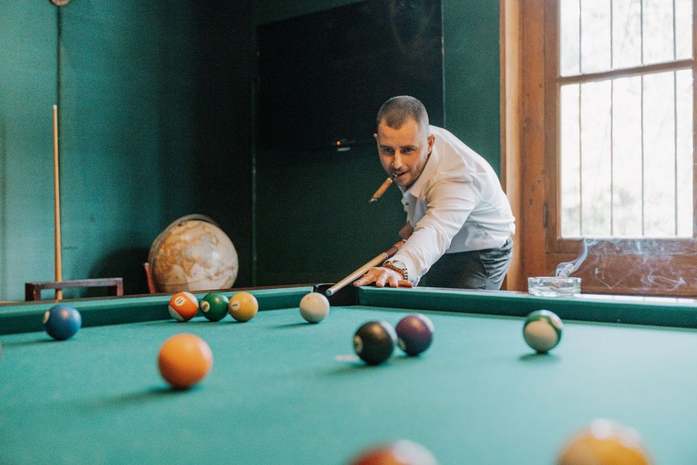 A person plays pool at a billiards table in a room with teal green walls.