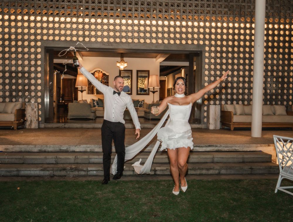 A joyful couple celebrates at sunset outside a venue with decorative lattice walls and a manicured lawn.