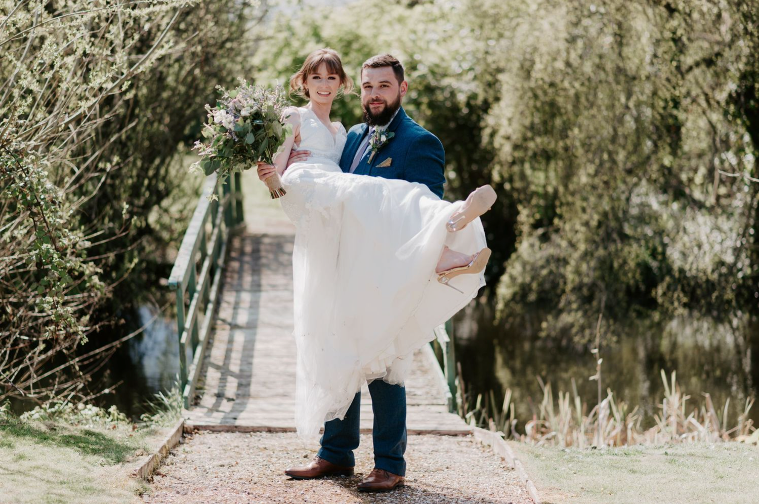 A couple in wedding attire dances together on a tree-lined outdoor path during a celebration.
