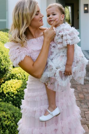 Mother and daughter in matching pink ruffled dresses share a tender moment outdoors.