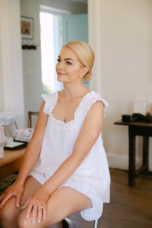 Person in white ruffled top sitting indoors near window with natural light.