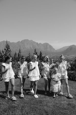 People in white vintage dresses standing in a line against a mountainous landscape in black and white.