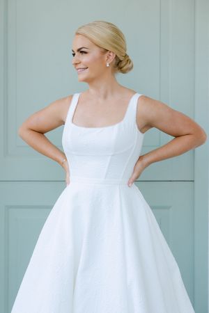 A classic white wedding dress with a fitted bodice and full skirt is shown against a mint green wall.