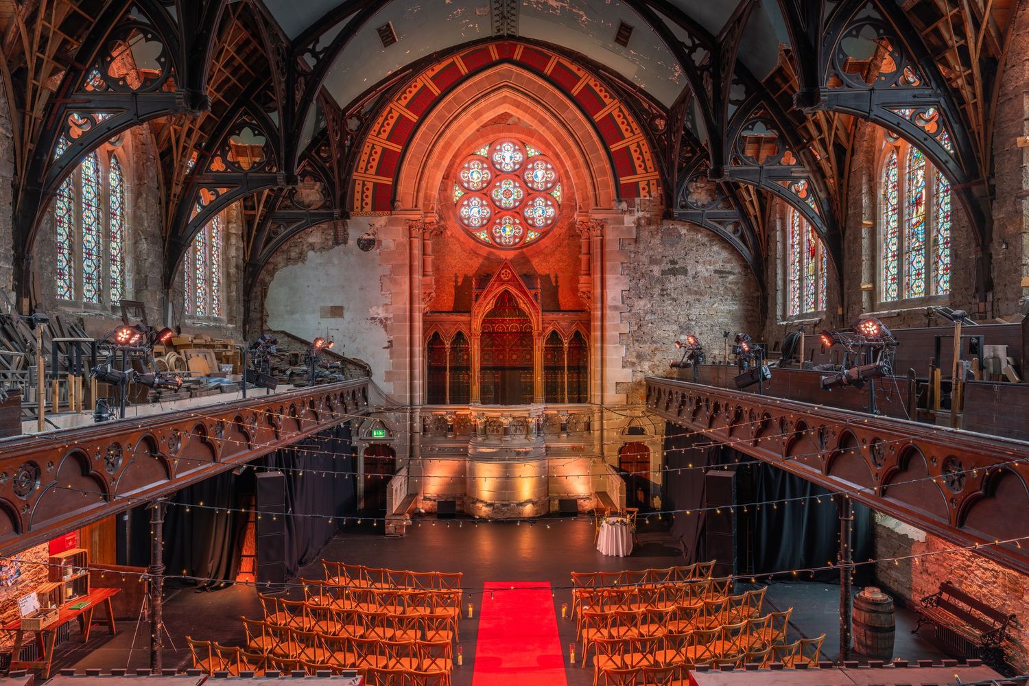 Gothic church interior with dramatic red lighting and rows of wooden chairs set up for a ceremony.