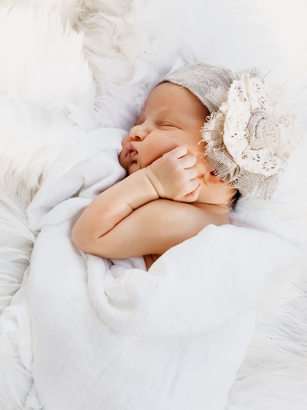 Peaceful sleeping newborn baby wrapped in white blanket wearing decorative floral headband.