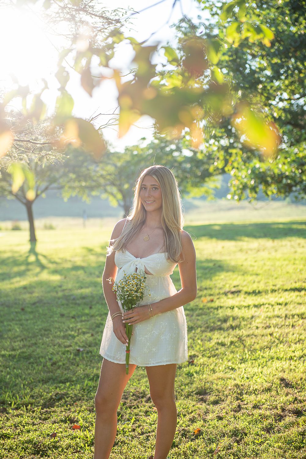 Sun-drenched outdoor photoshoot in a grassy field with white summer clothing and natural lighting.