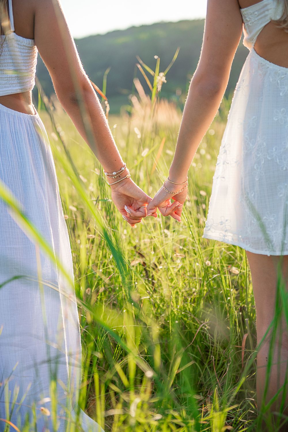 White-dressed figures gently touch wildflowers in a sunlit meadow during golden hour.