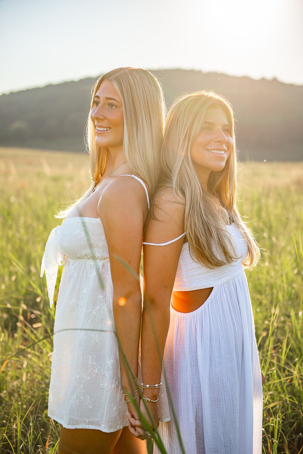 Friends share laughter in a golden field at sunset wearing white summer outfits.
