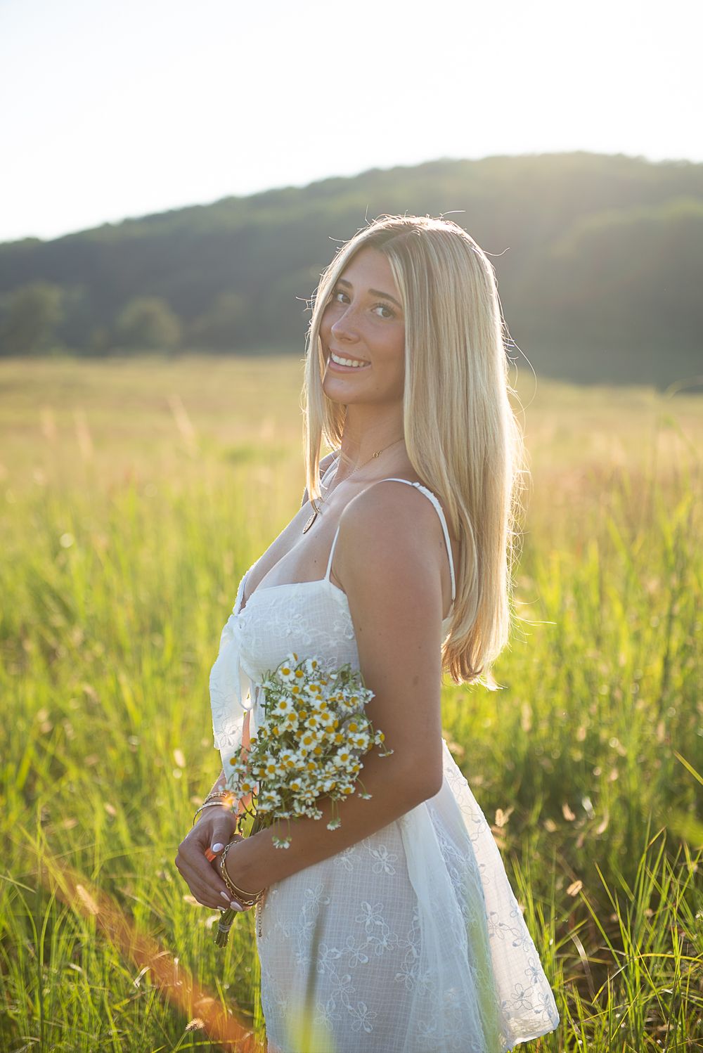 Person in white dress holds delicate wildflowers in a sun-drenched summer field.