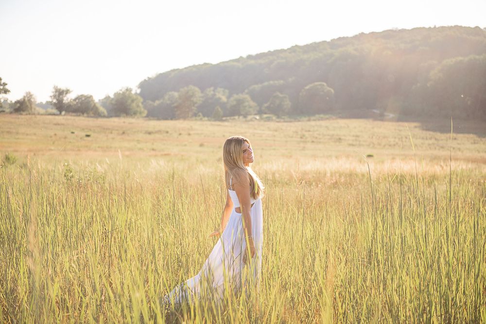 Two figures stroll through a serene meadow landscape bathed in warm evening sunlight.