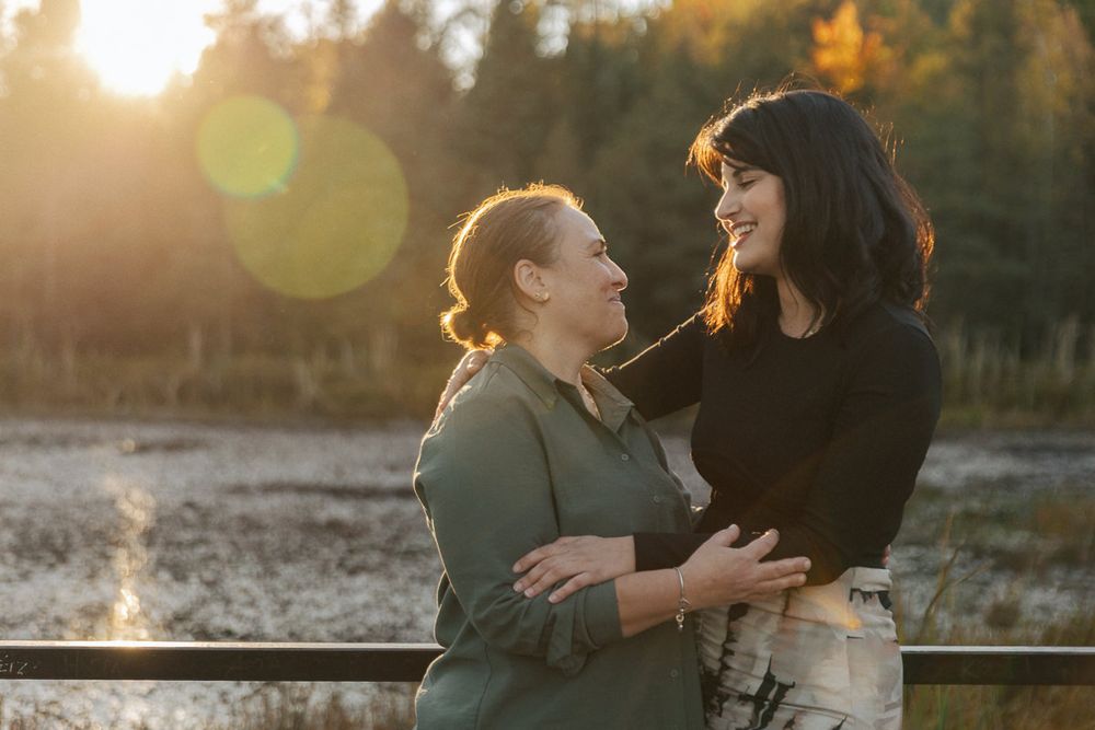 A couple embraces in golden sunset light by a waterfront with lens flare effects.