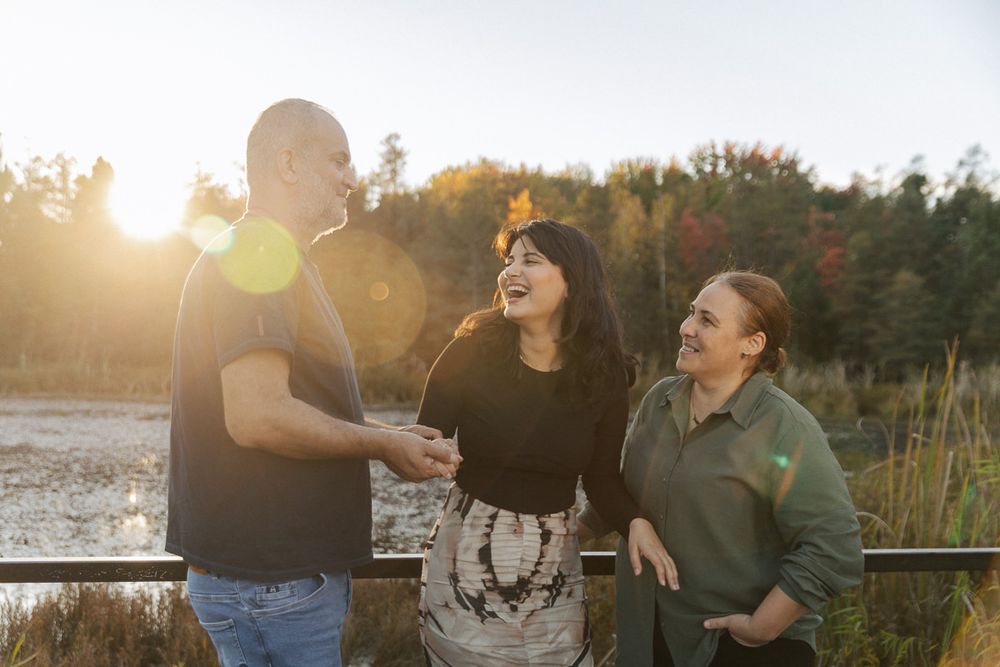 Three friends sharing laughter together at sunset by a wooden railing outdoors.