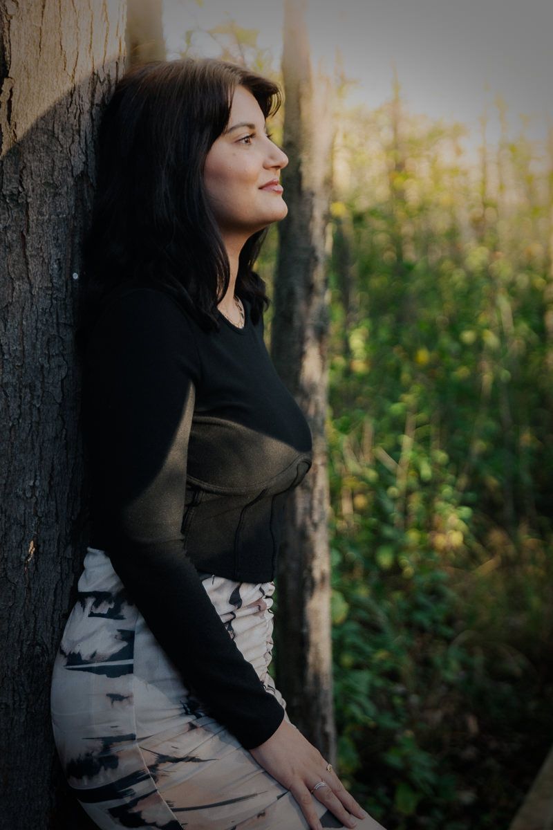 Artistic portrait series showing a dark-haired figure in black against a tree with natural sunlit background.