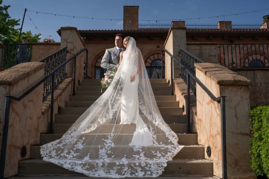 A flowing wedding dress train with delicate lace details trails down stone steps at The Club at Corazón