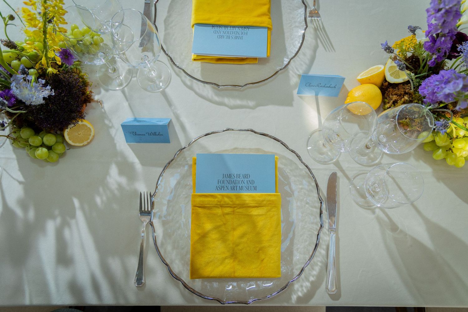 Elegant table settings with yellow menu cards, white linens, and purple floral centerpieces at a formal event.