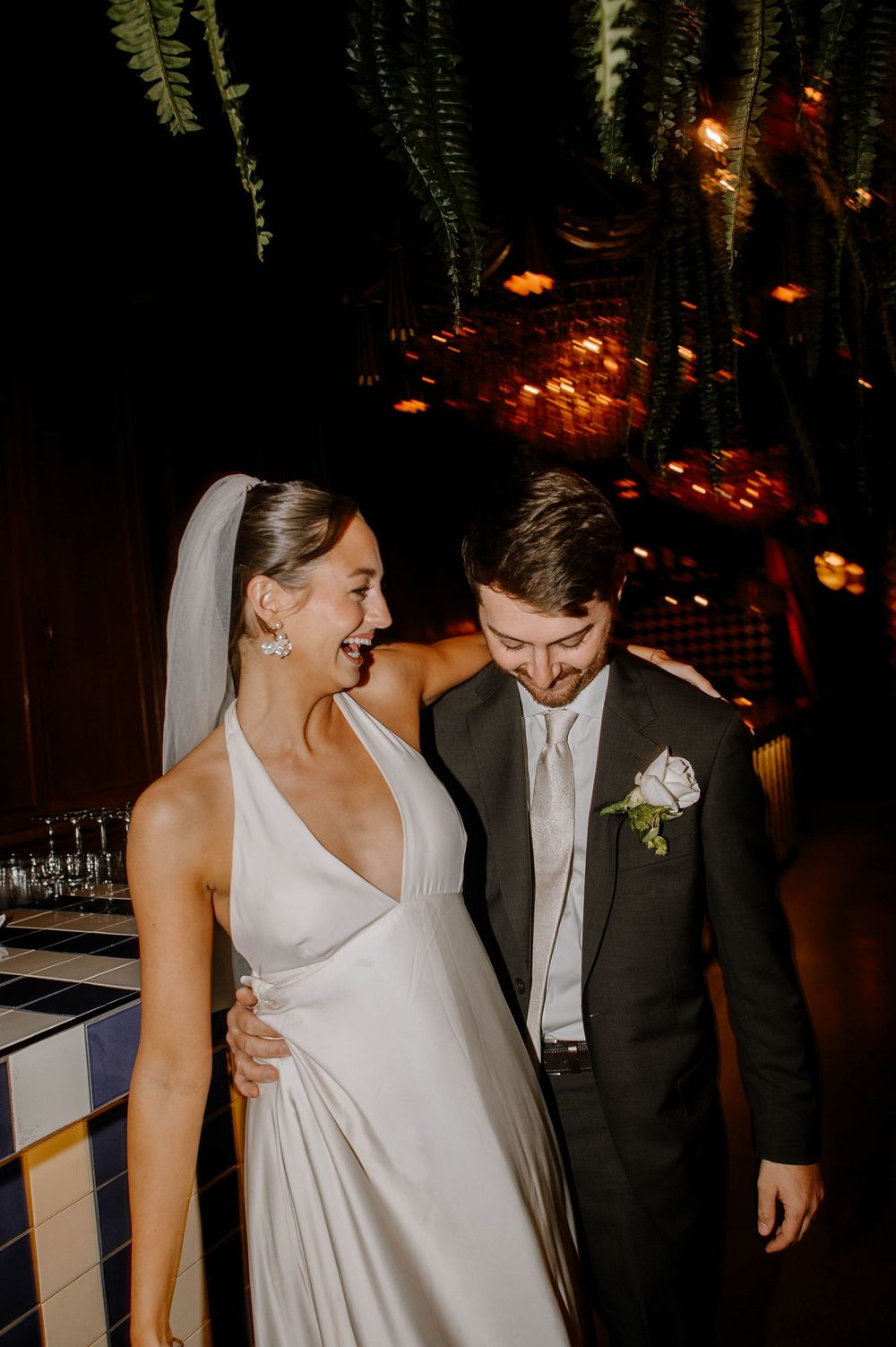 Newlyweds share a joyful moment under warm lighting at an evening wedding reception.