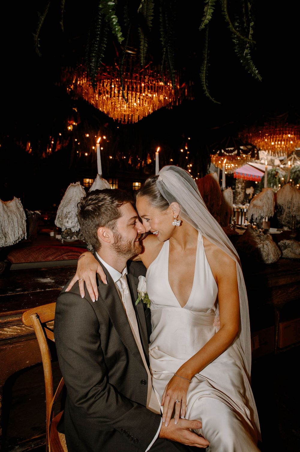 Romantic couple embraces during their wedding reception under glowing chandeliers.