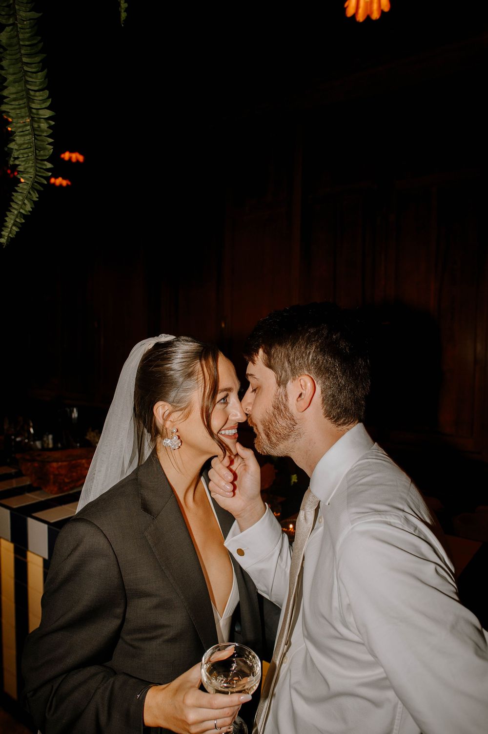 Intimate wedding moment captured in low light with hanging greenery overhead.