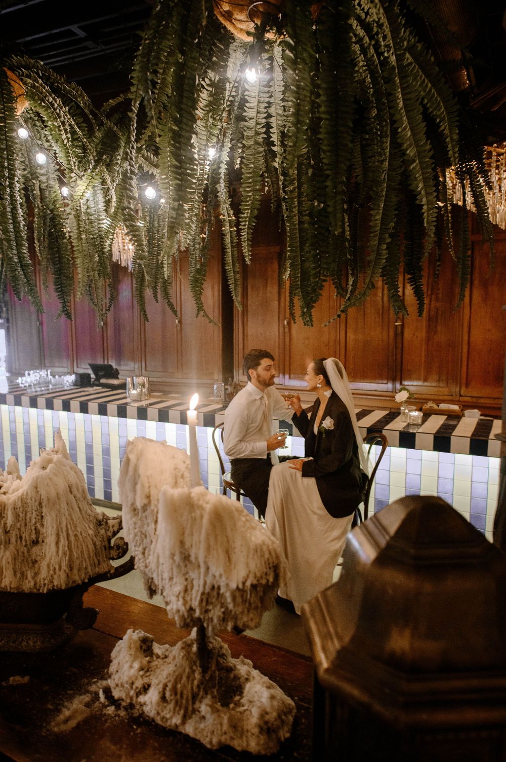 Wedding reception venue decorated with hanging ferns and white draping creates an enchanted atmosphere.
