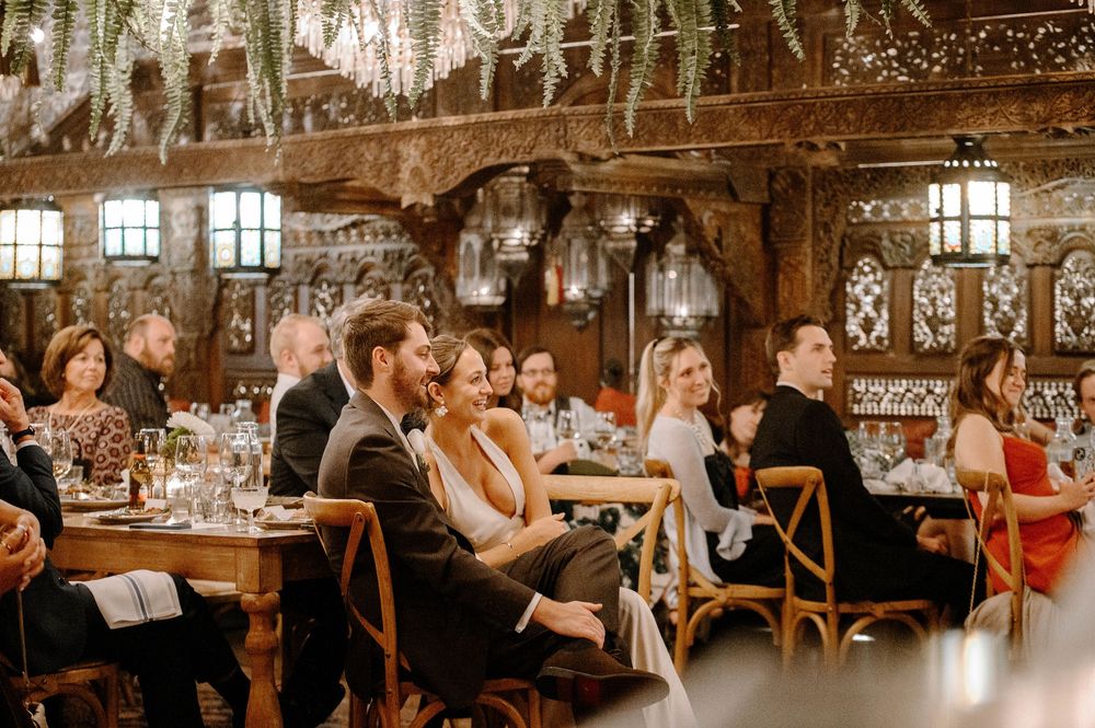 Wedding guests dance and celebrate in a rustic barn venue decorated with string lights and wooden beams.