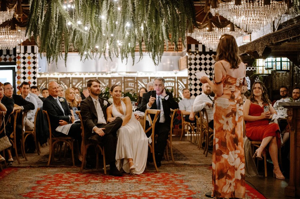 Wedding guests dance and celebrate under romantic string lights and chandeliers at an elegant reception venue.