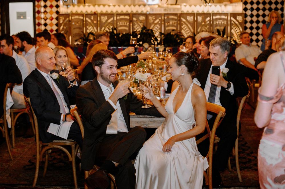 Wedding reception guests dancing and celebrating on a crowded dance floor under elegant chandeliers.