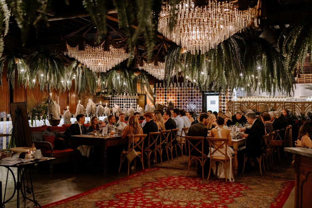 Elegant wedding reception venue with crystal chandeliers and white floral arrangements illuminated in warm lighting.
