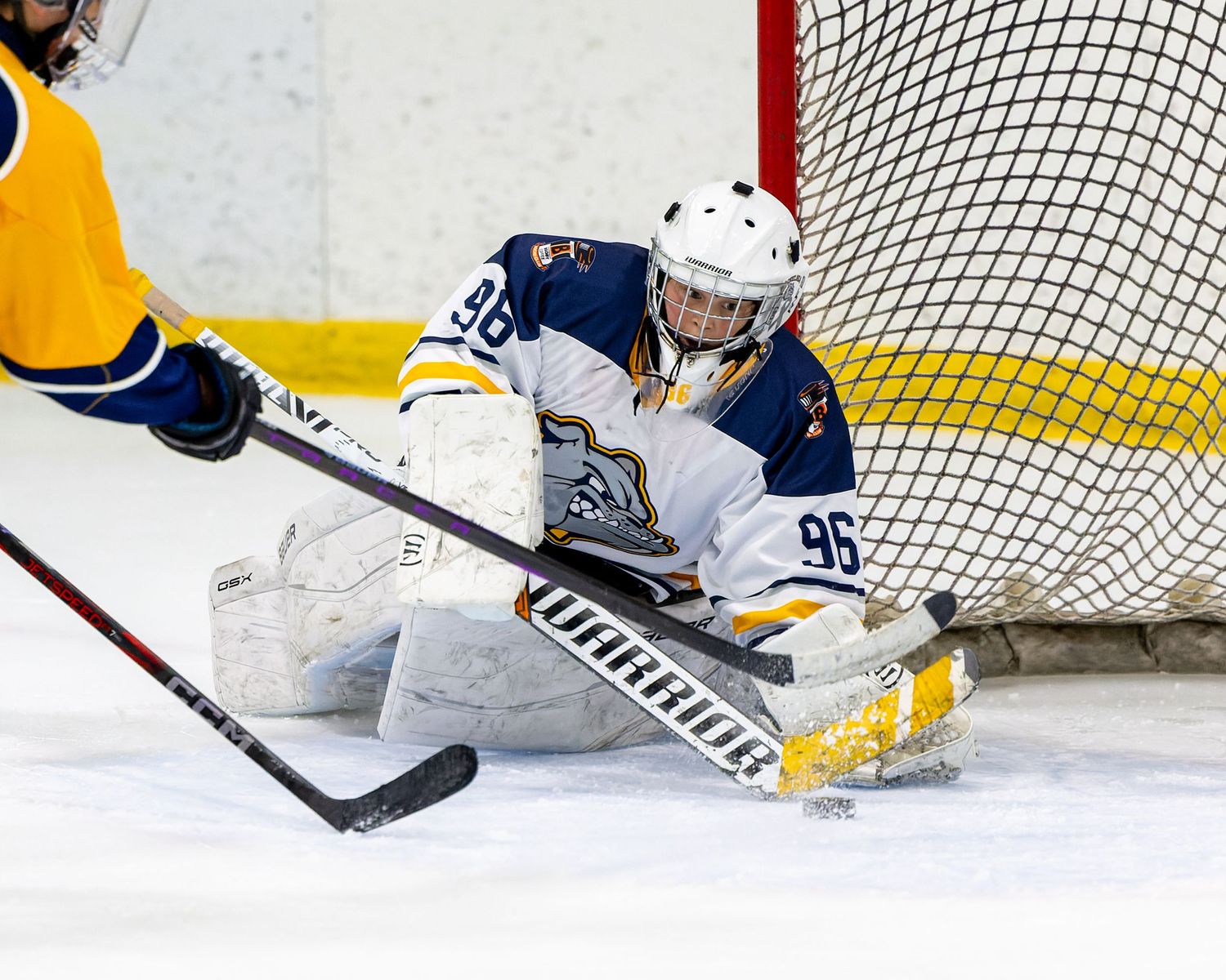 Hockey player stretches to make a save as the puck slides toward the goal during an intense game moment.