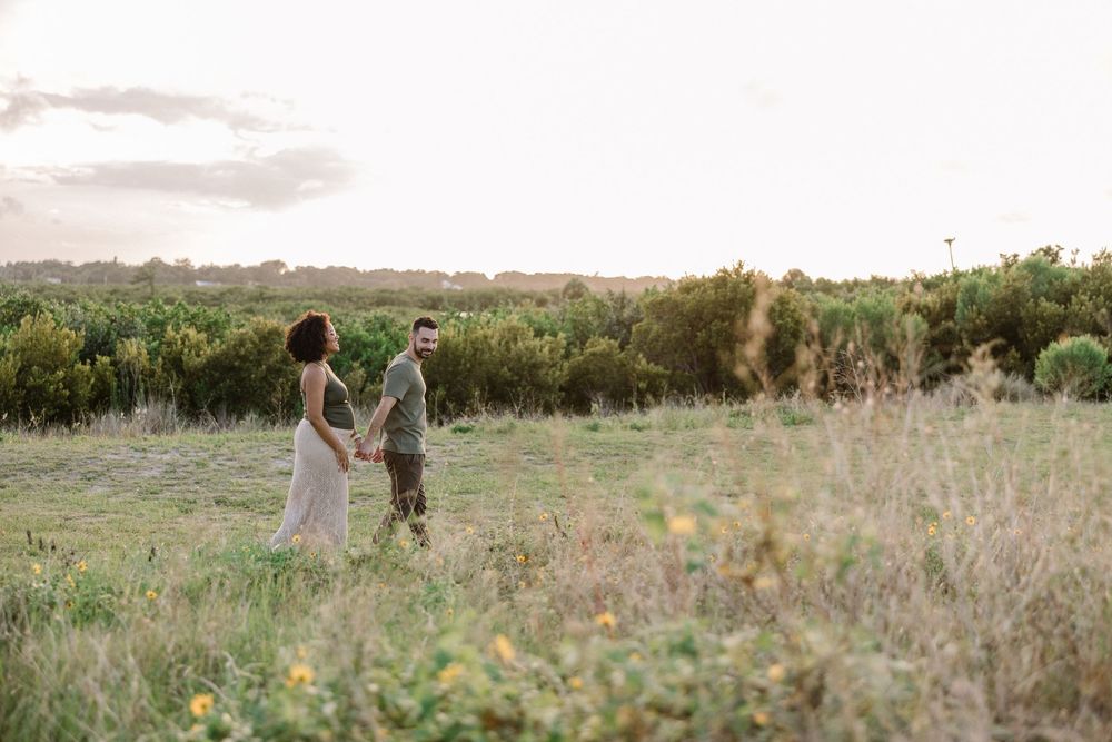 A couple walks through a golden field at sunset holding hands during an outdoor photoshoot session.