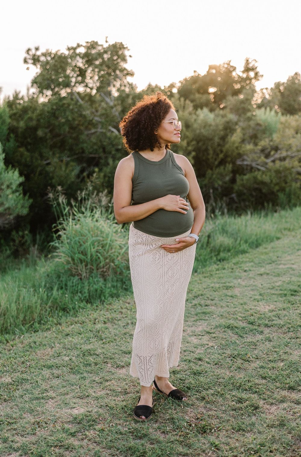 A person in a green top and flowing beige skirt dances gracefully in a grassy field at sunset.