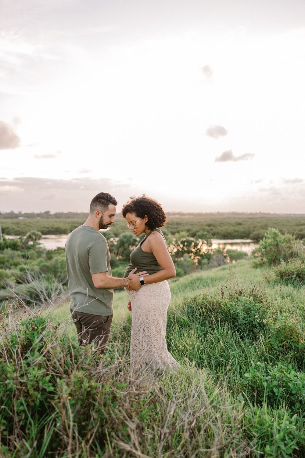 A couple shares an intimate moment together in a lush green field at sunset.
