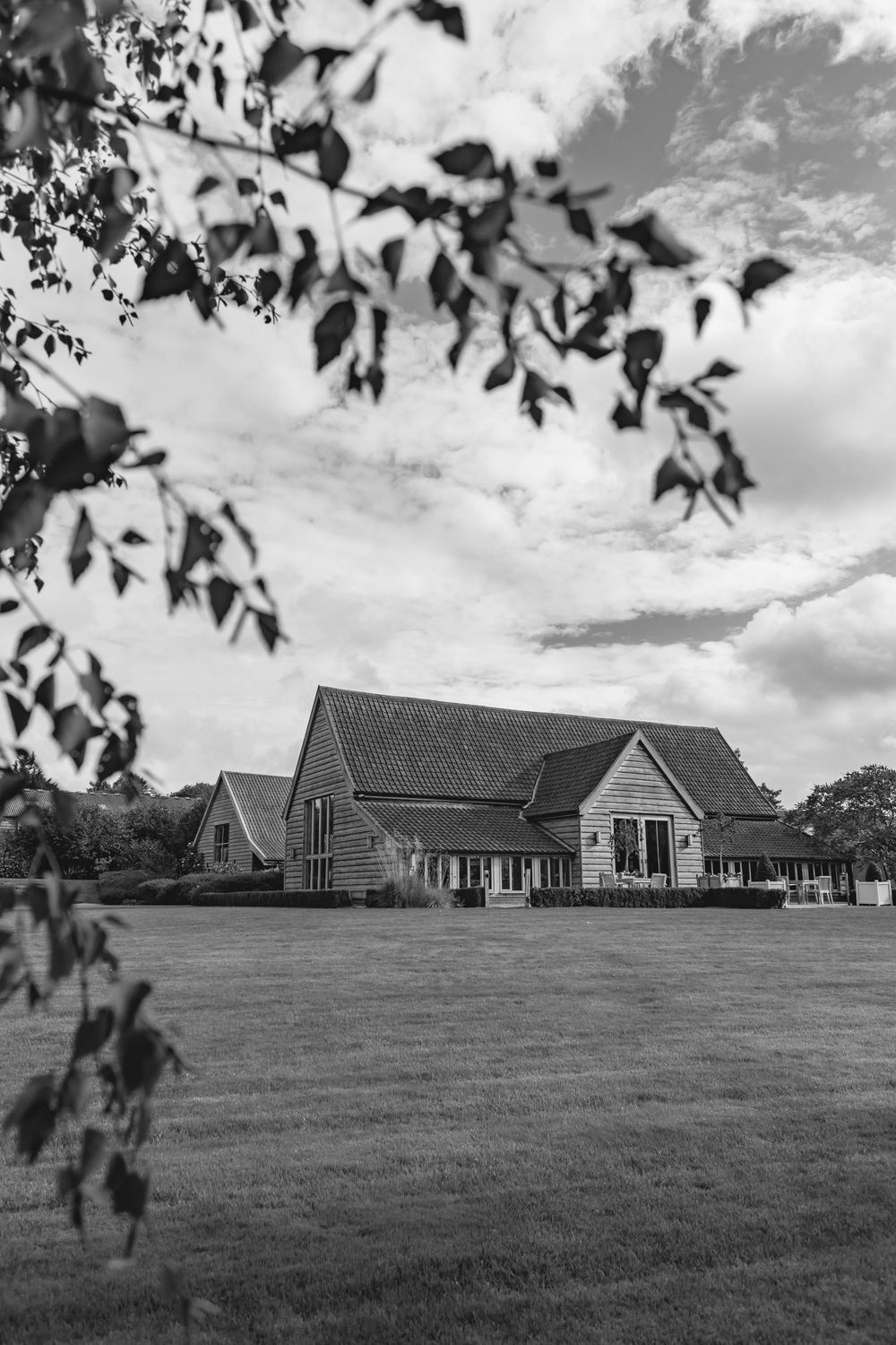 Black and white landscape view of modern wedding venue buildings on grassy hillside.