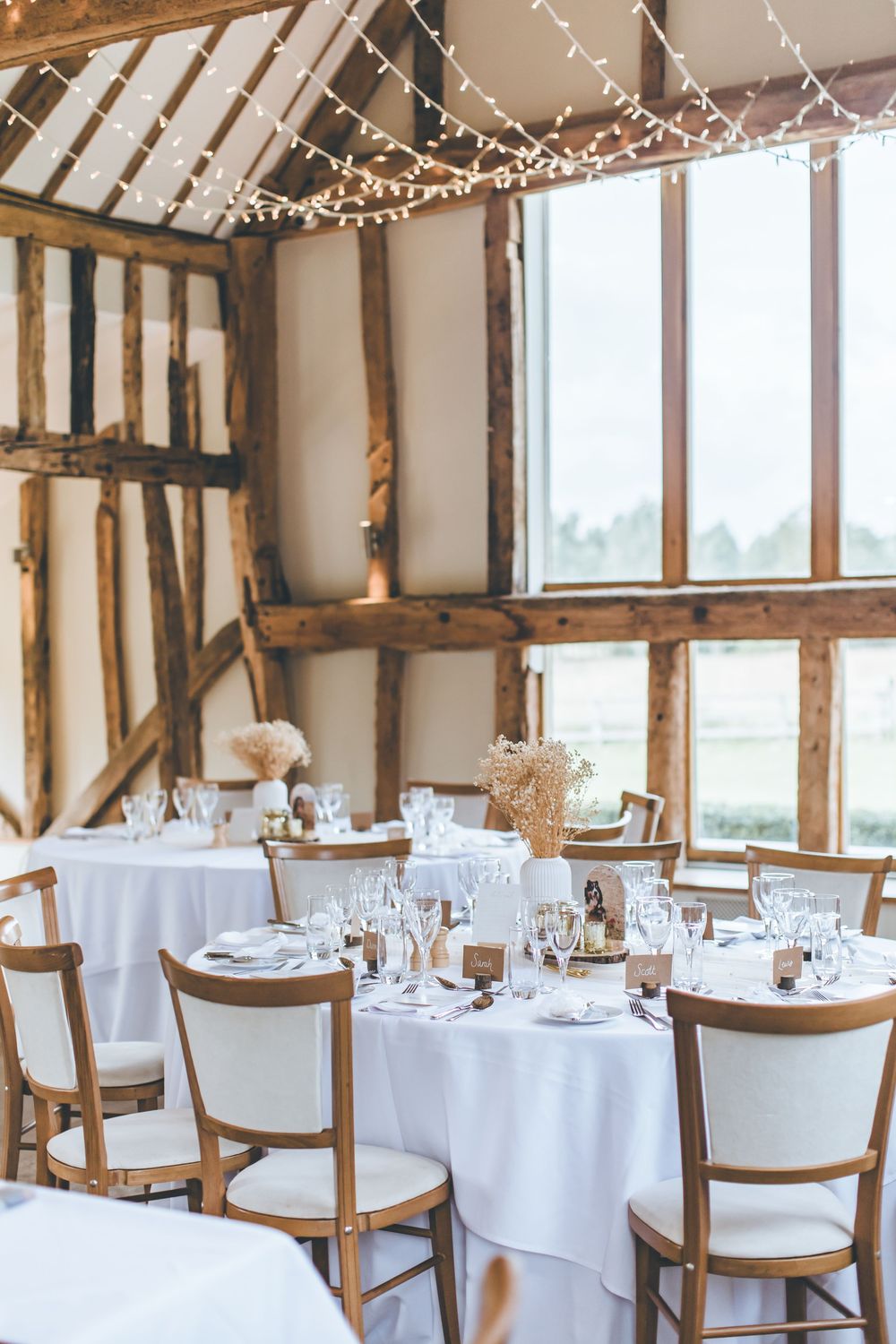 Elegant wedding reception setup in rustic barn with exposed beams and string lights.