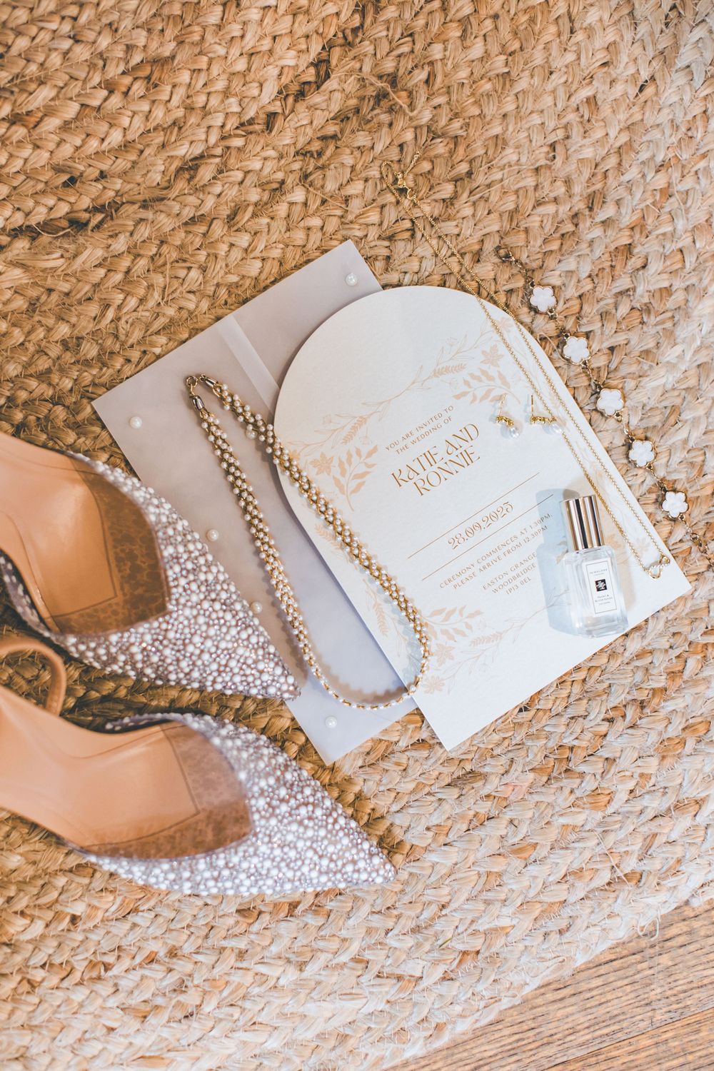 Wedding details including invitations, pearls, and shoes arranged on a textured woven surface.