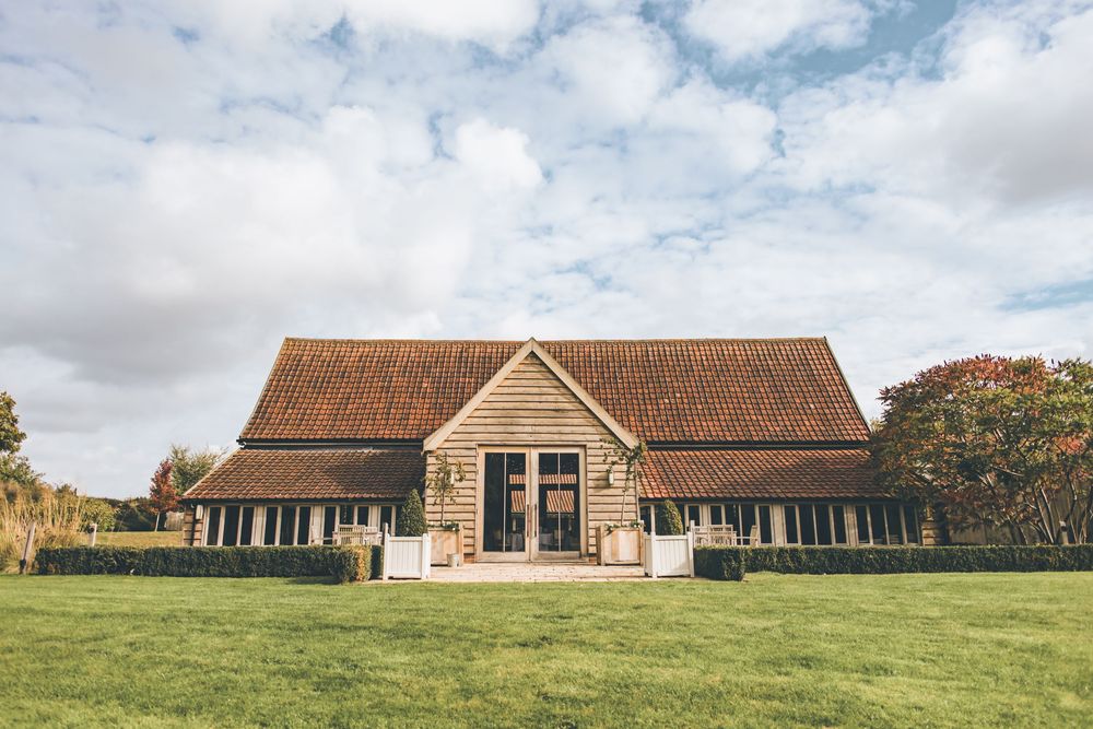 Panoramic view of rustic wedding venue buildings with green lawn and cloudy sky.